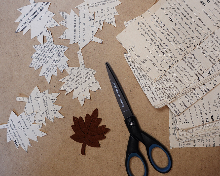 Javorové listy povystrihované pomocou nožníc zo strán knižky matematiky, ležia na sololite.